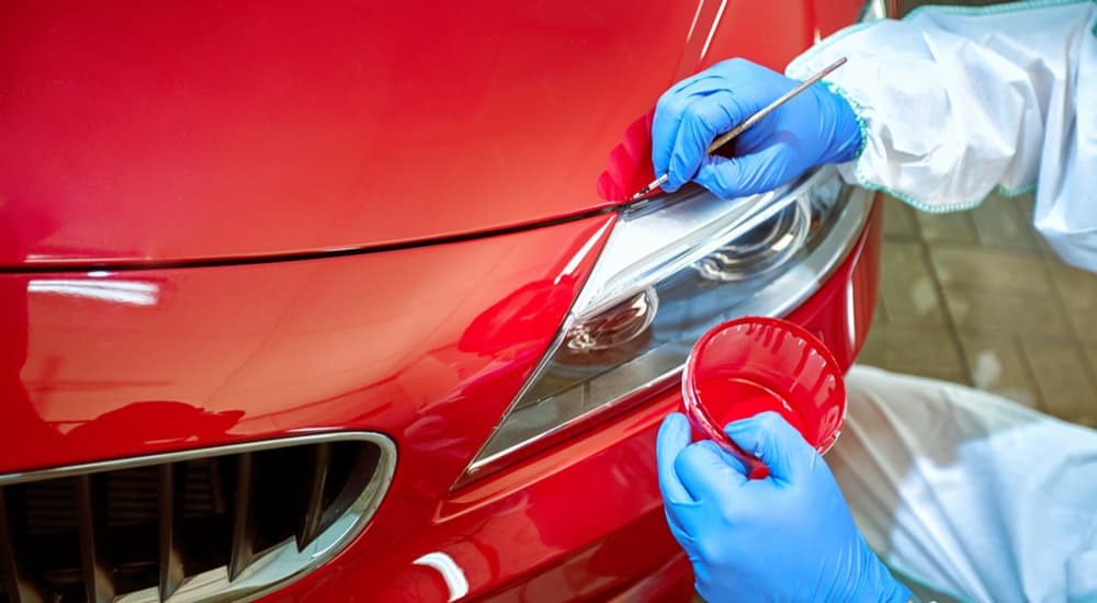 A person is shown touching up paint near the headlight of a red car.