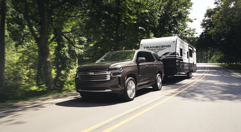 A grey 2021 Chevy Tahoe High Country is shown towing a trailer down a wooded road.