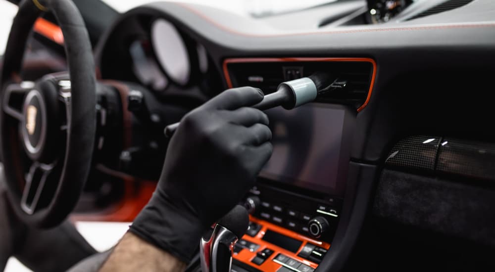 A person is shown using a brush to clean the center console of a vehicle.