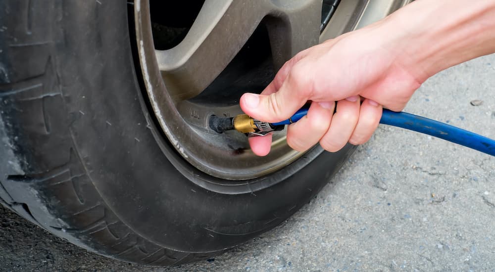 A close up shows a person filling a tire with air before visiting a used car dealership.