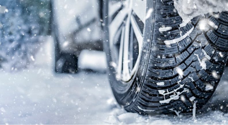 A close up shows a winter tire driving in snow.