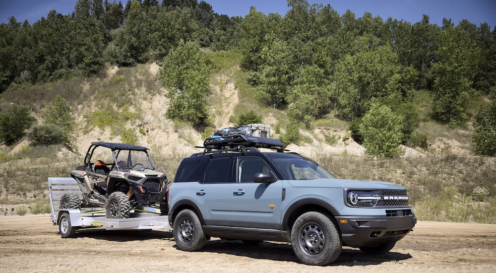 A light blue 2022 Bronco Sport is shown from the side hooked up to a trailer that is loaded with a Polaris Ranger RZR.
