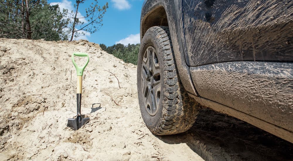 A shovel is shown in the dirt next to a muddy tire.