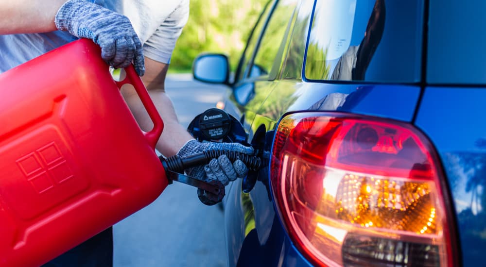 A person is shown using a red gas can to fill the tank of a blue vehicle.