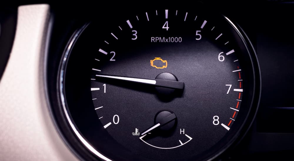 A close up shows and illuminated check engine light on a tachometer.