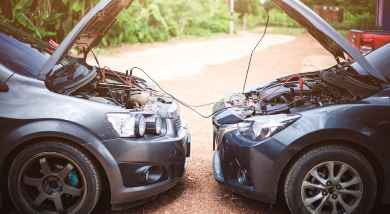 Two cars are shown from the side facing each other with jumper cables attached to their batteries.