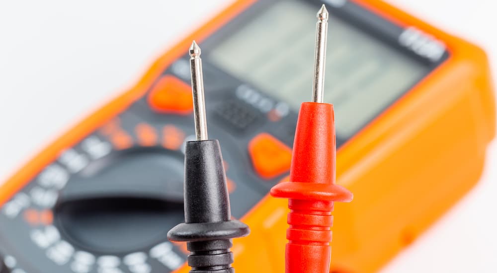 A close up shows multimeter probes with a blurred multimeter in the background.