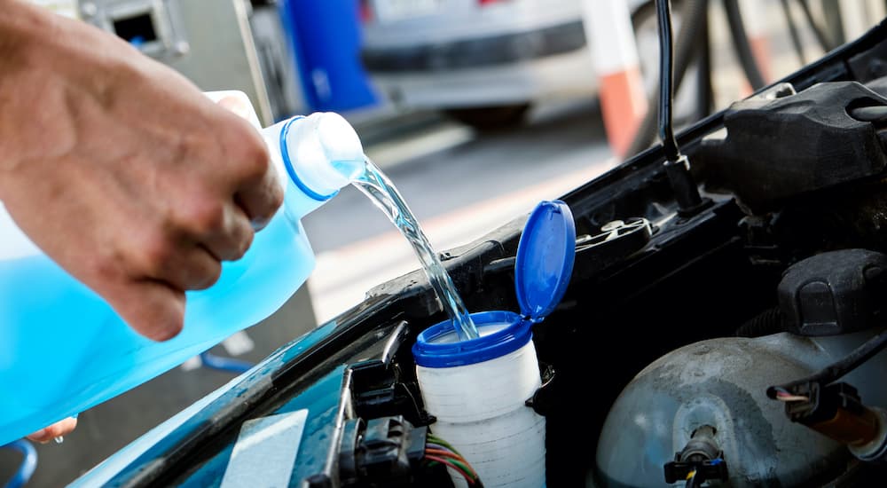 A person is shown filling a reservoir with windshield washer fluid.