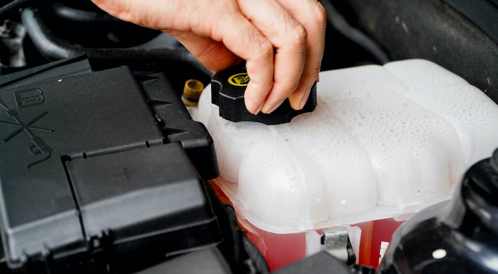 A close up shows a hand opening a coolant reservoir.