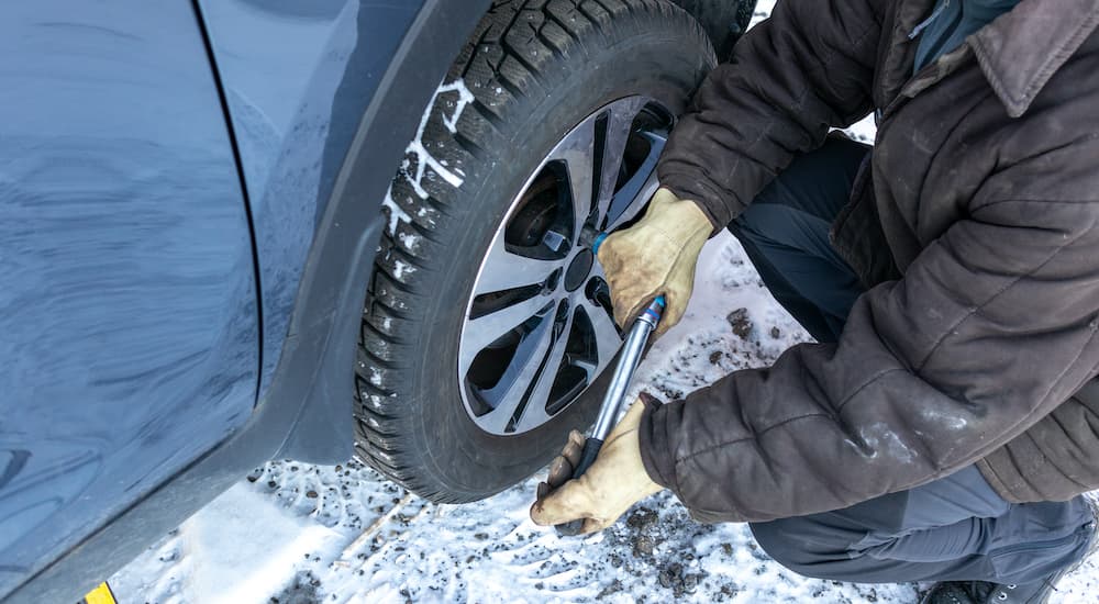 A person is shown changing a tire in the snow.