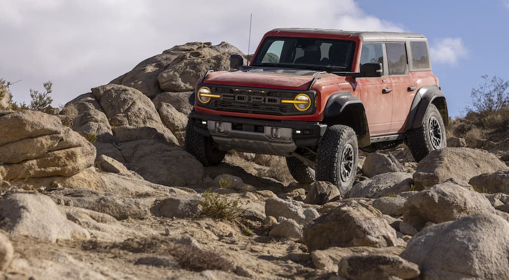 A red 2022 Ford Bronco Raptor is shown from the front at an angle while crawling over rocks.