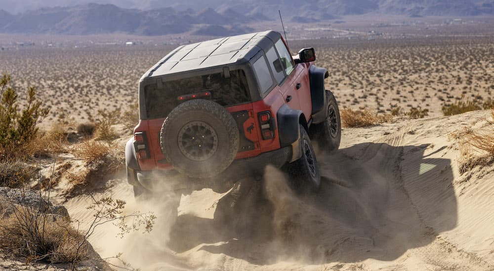 A red 2022 Ford Bronco Raptor is shown from the rear while it kicks up sand.