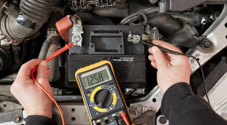 A person is shown testing voltage on a car battery with a multimeter.