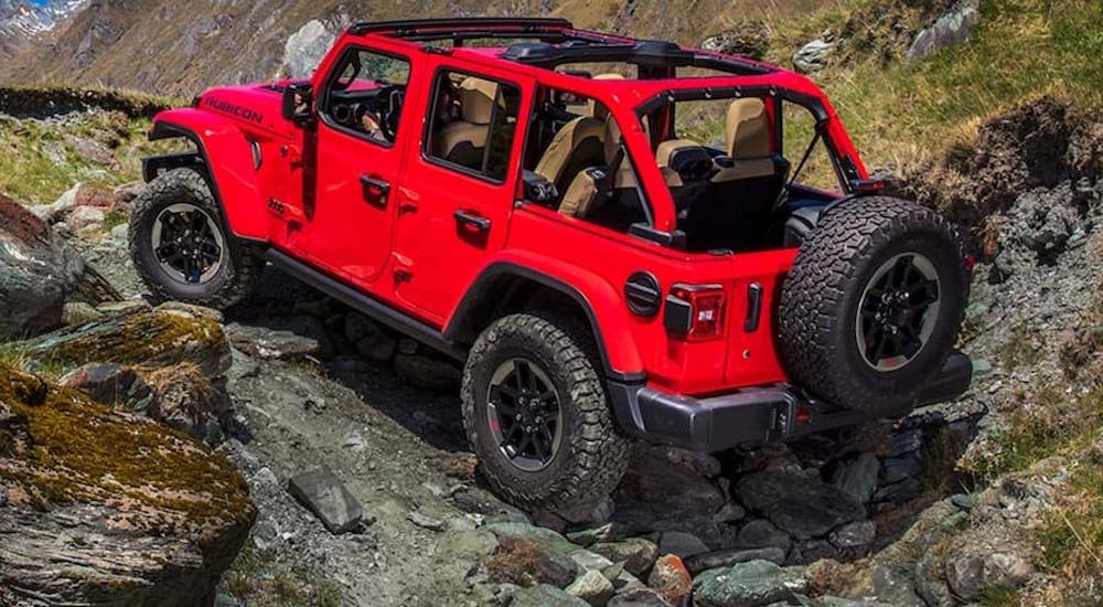 A red 2020 Jeep Wrangler Unlimited Rubicon is shown from the rear at an angle while it traverses a rocky area.