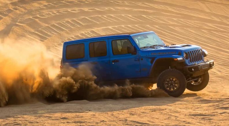 A blue 2021 Jeep Wrangler Rubicon 392 is shown from the side driving through the sand after the owner searched 'Jeep parts Colorado Springs'.