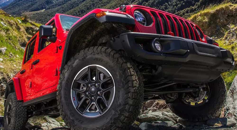 A red 2022 Jeep Wrangler Unlimited Rubicon is shown from the front at a low angle as it crawls up a rocky hill.