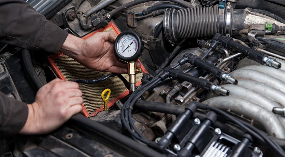 A hand is shown holding a compression tester in an engine bay.