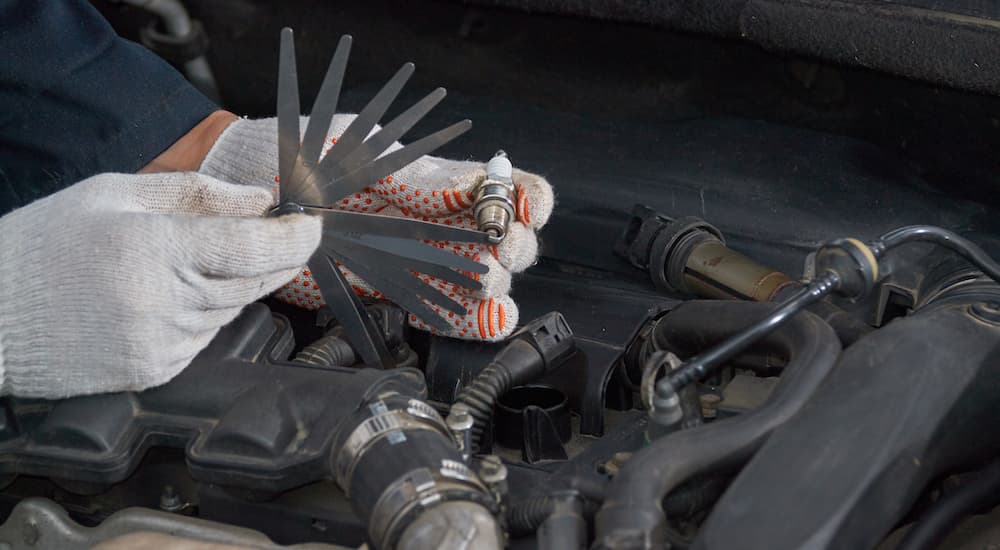 A close up shows gloved hands using a gauge to check spark plug gap.