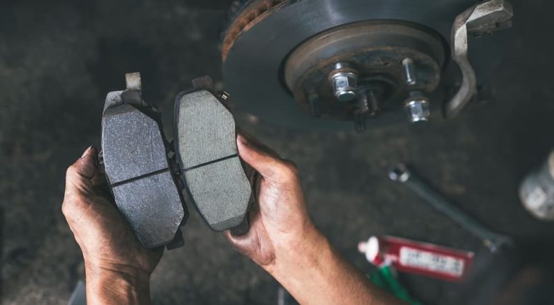 A person is shown holding a set of brake pads during a brake service.