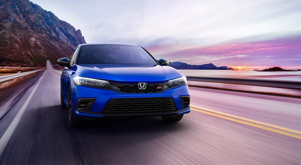 A blue 2022 Honda Civic Si is shown driving on a coastal road on the way to get a Honda service.