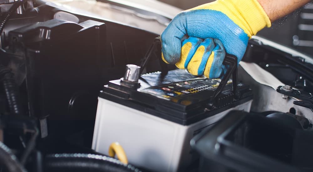 A mechanic is shown taking a car battery out of a vehicle.