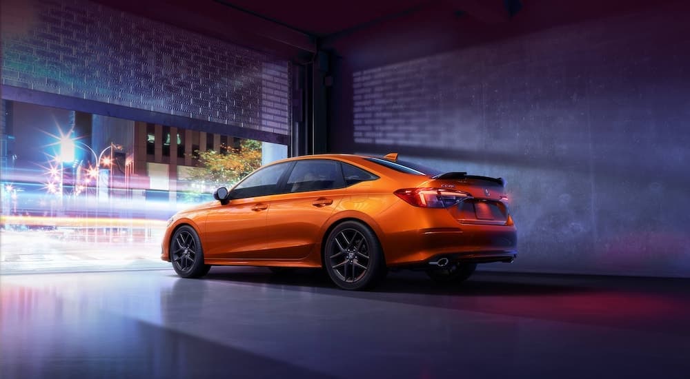 An orange 2022 Honda Civic Si is shown from behind in an urban area.