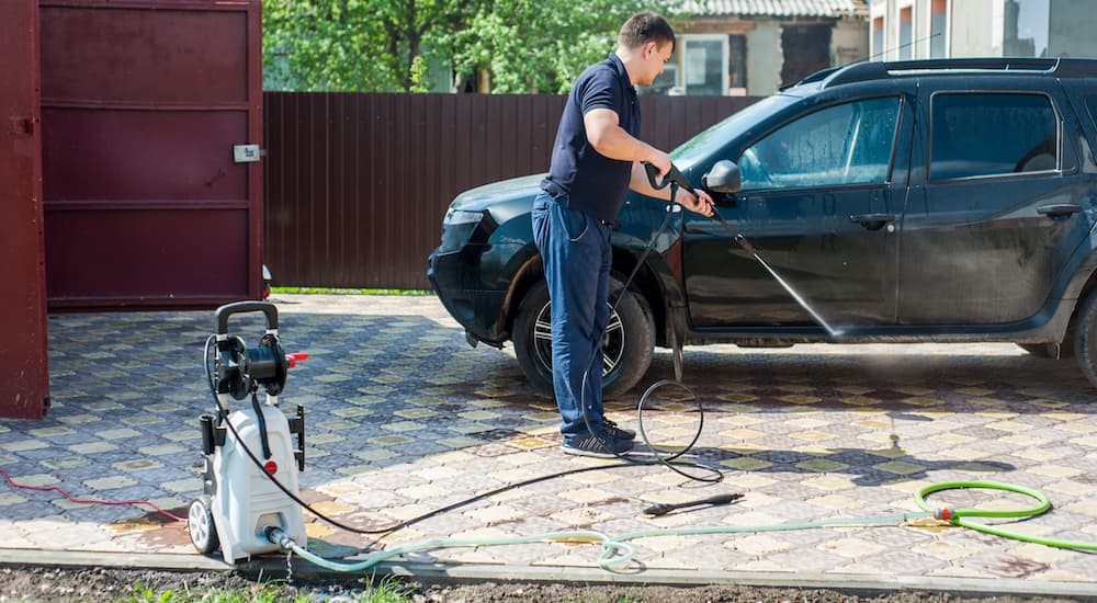 A person is shown using a pressure washer to clean their vehicle in a driveway.