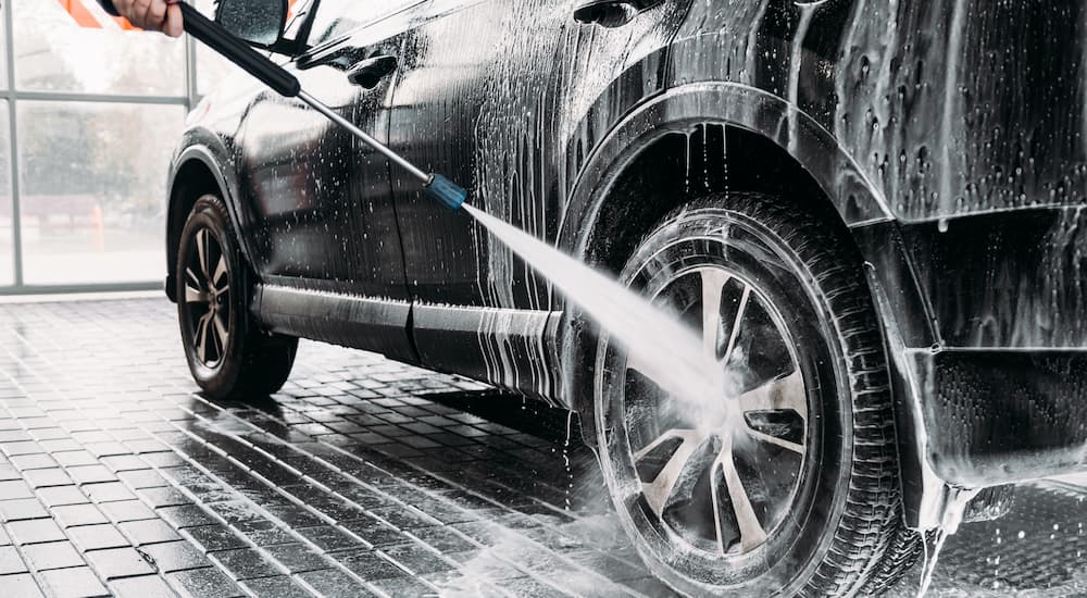 A person is shown pressure washing the tire of a black vehicle.