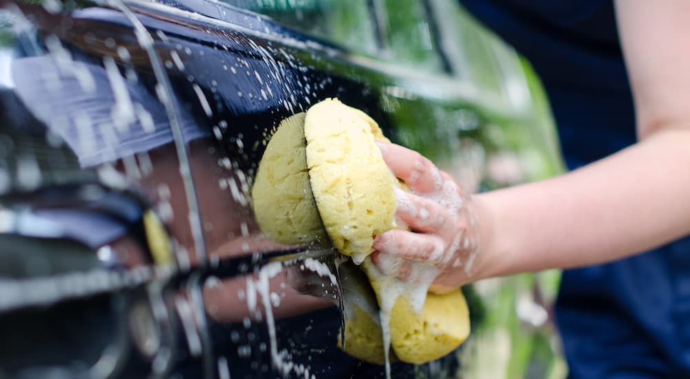 A person is shown washing the side of a car with a yellow sponge.
