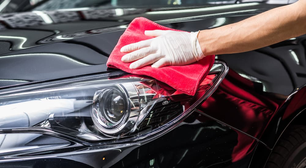 A gloved hand is shown waxing the hood of a black vehicle.