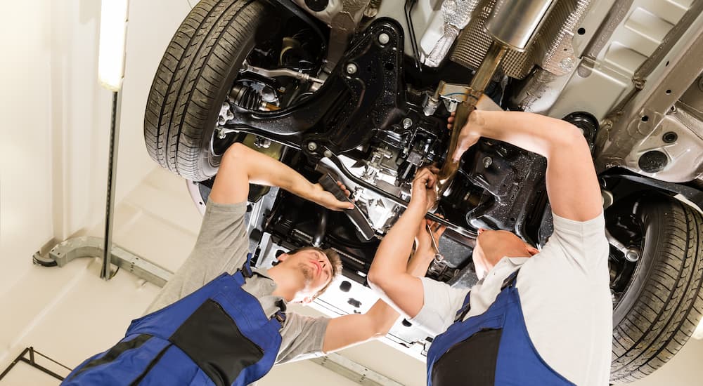 Two mechanics are shown looking at the bottom of a vehicle on a lift.