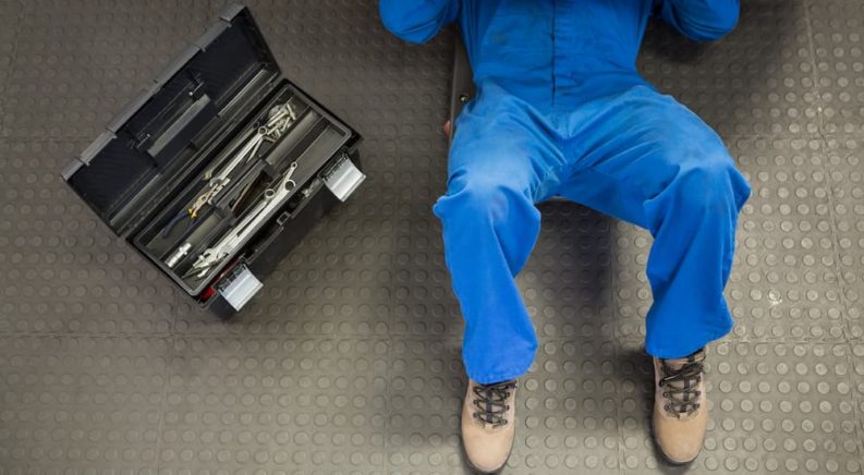 A mechanic is shown on lying on the ground underneath a vehicle.