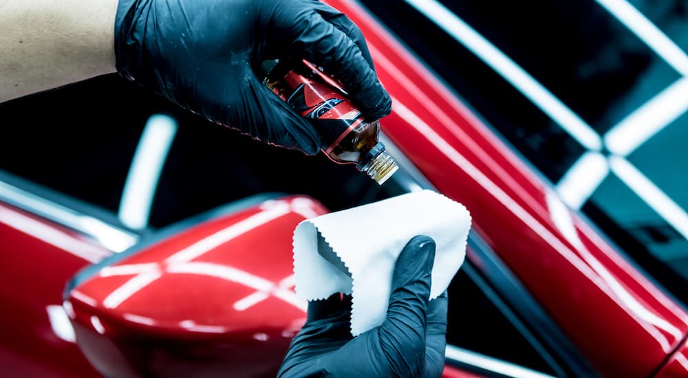 A person is shown applying ceramic coating to a pad in front of a red 2013 Mazda6.