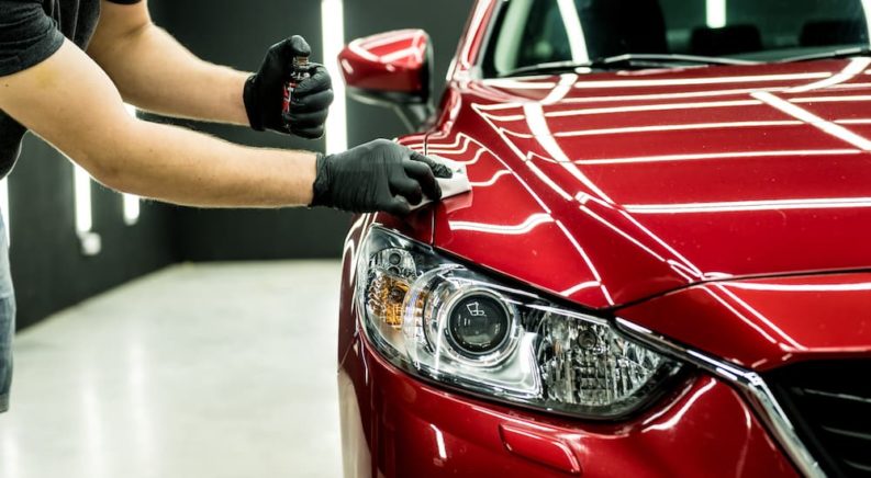 A person is shown applying ceramic coating to the hood of a red 2013 Mazda6.