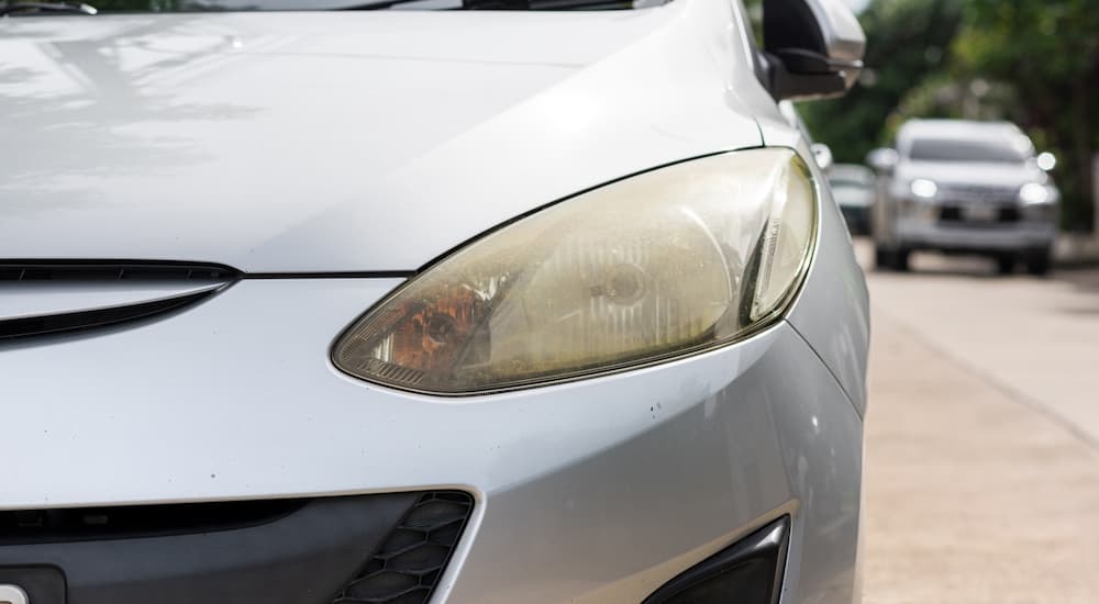 A close up shows an oxidized headlight on a silver 2012 Mazda 2.