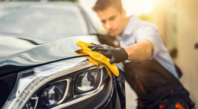 A man is shown using a yellow rag to wipe down a black sedan.