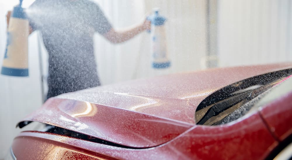 A person is shown spraying wax onto a red car.