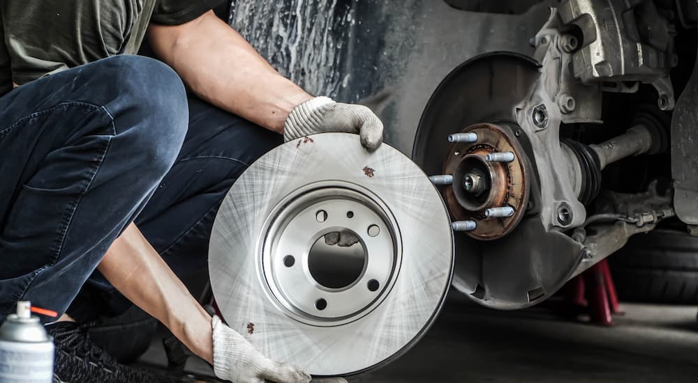 A mechanic is shown holding a rotor next to a vehicle during a brake service.