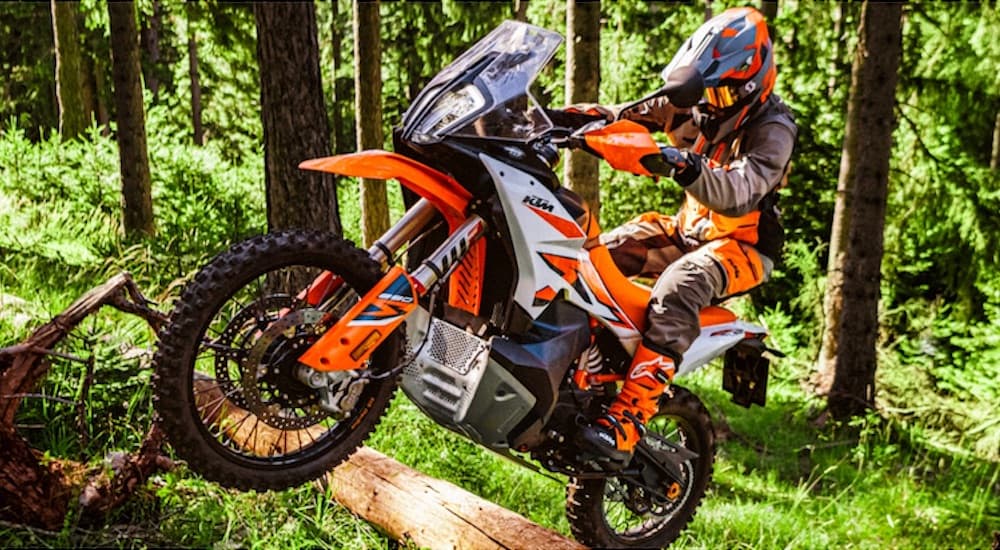 An orange 2022 KTM 890 Adventure R is shown jumping through the forest.