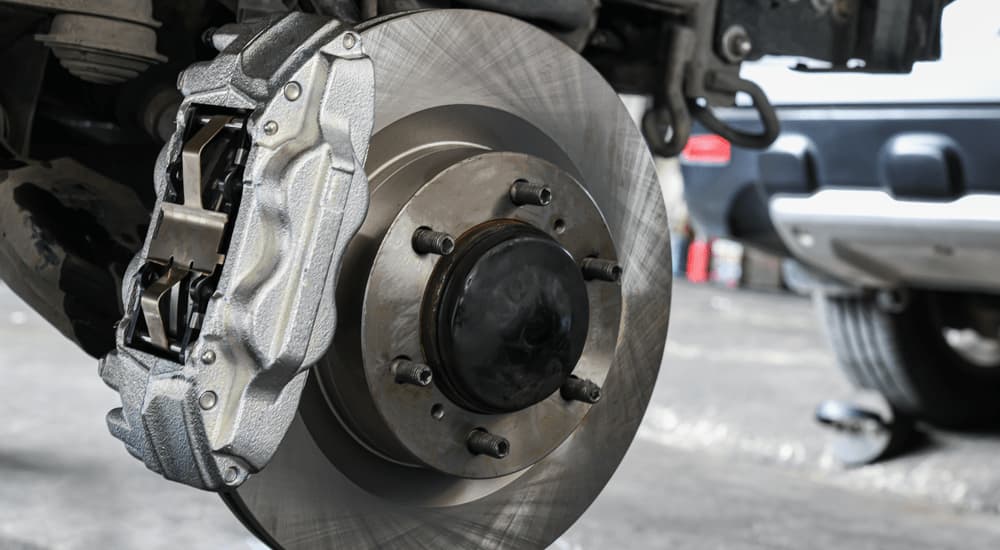 A close up of a vehicle's brake caliper and rotor is shown at a repair shop.