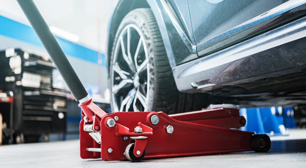 A red car jack is shown underneath a vehicle.