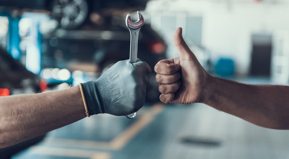 A gloved hand and a non-gloved hand are shown giving a thumbs up in a mechanic's shop.