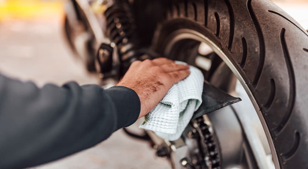 Someone is shown wiping down a motorcycle's chain guard.
