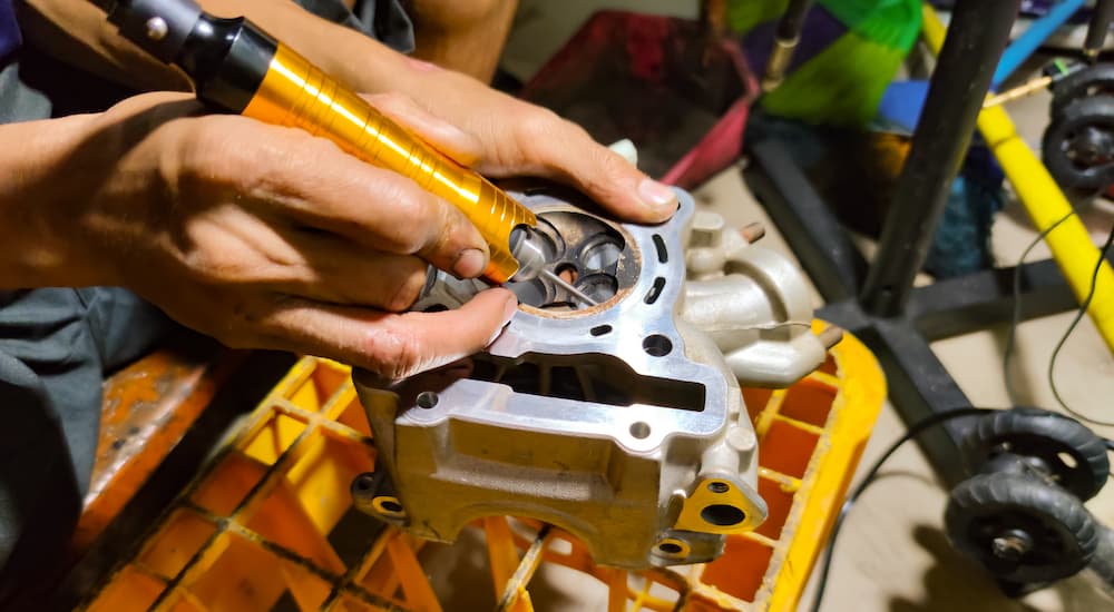 A mechanic is shown working on a cylinder head with a Dremel tool.