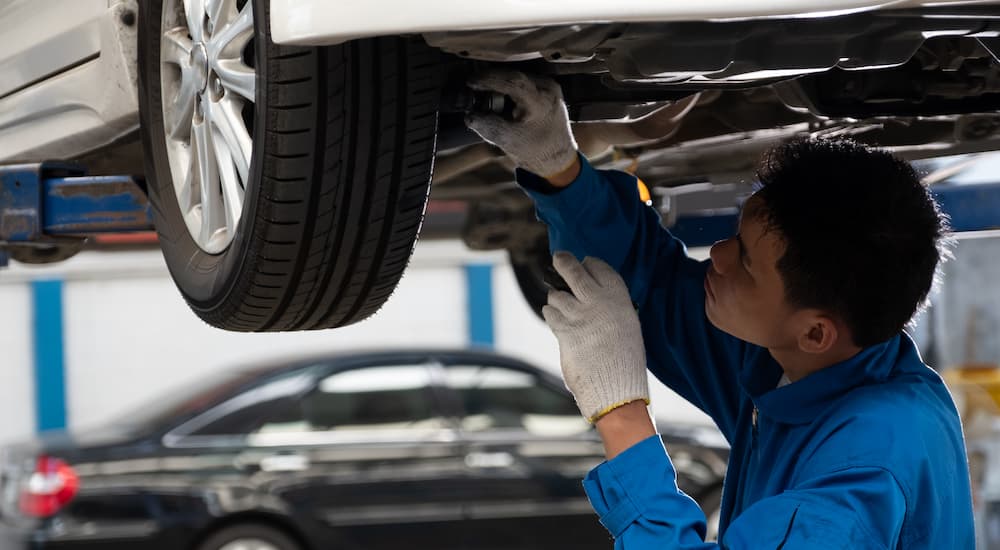 A mechanic is shown inspecting the underneath of a vehicle.
