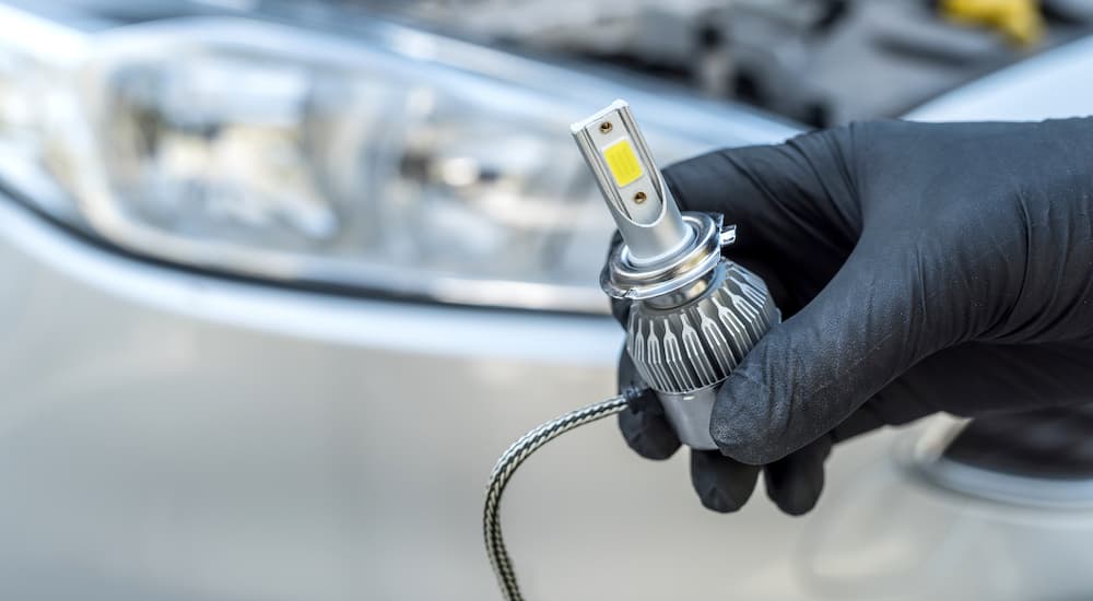 A gloved hand is shown holding an LED headlight bulb.