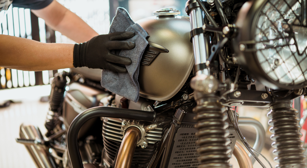 A mechanic is shown wiping the tank of a bronze motorcycle.