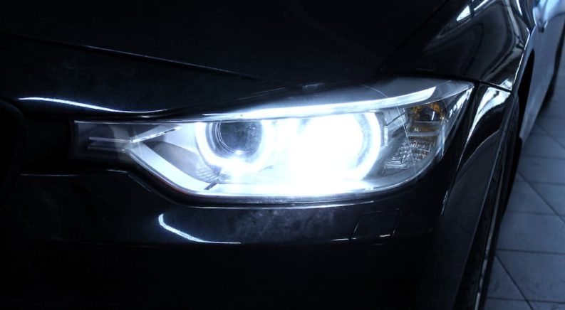 A close up shows in illuminated headlight on a black vehicle.