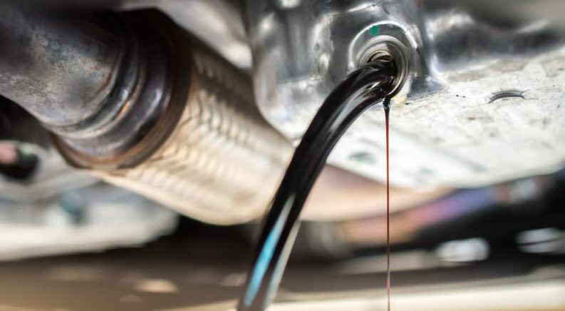 A close up shows oil being drained from an oil pan.