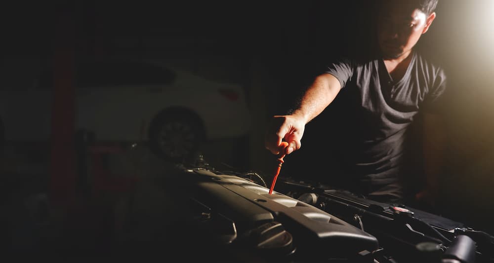 A person is shown pulling a dipstick out of a crankcase.